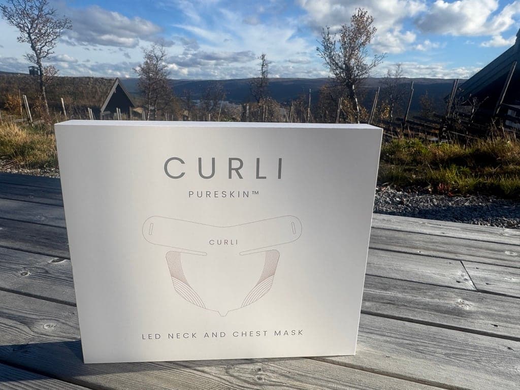 Esken til CURLI PureSkin LED Neck and Chest Mask på et trebord utendørs