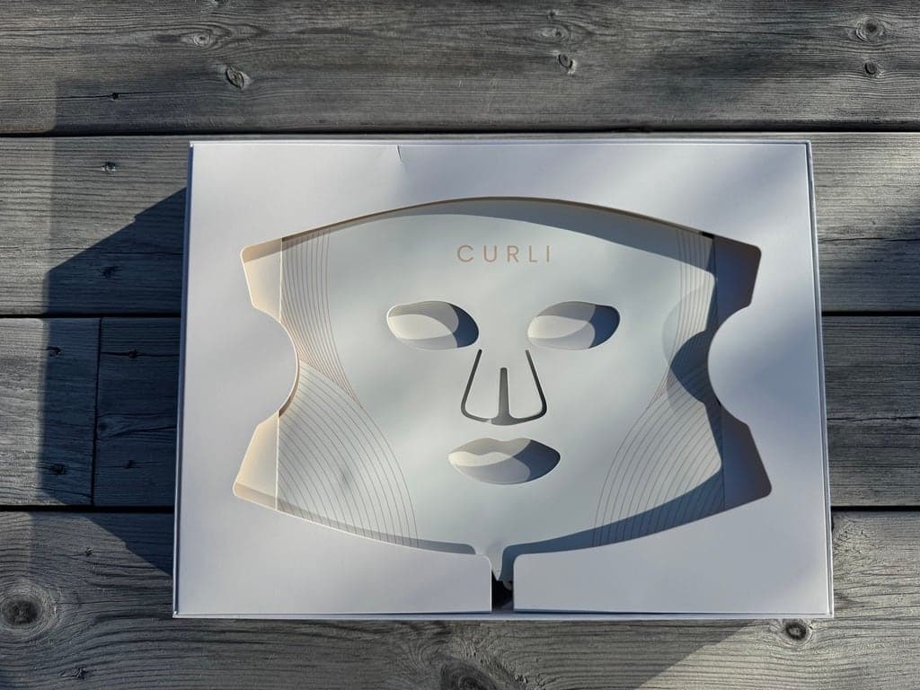 Ansiktsmasken liggende i utsparingen i esken, sett ovenfra på et trebord