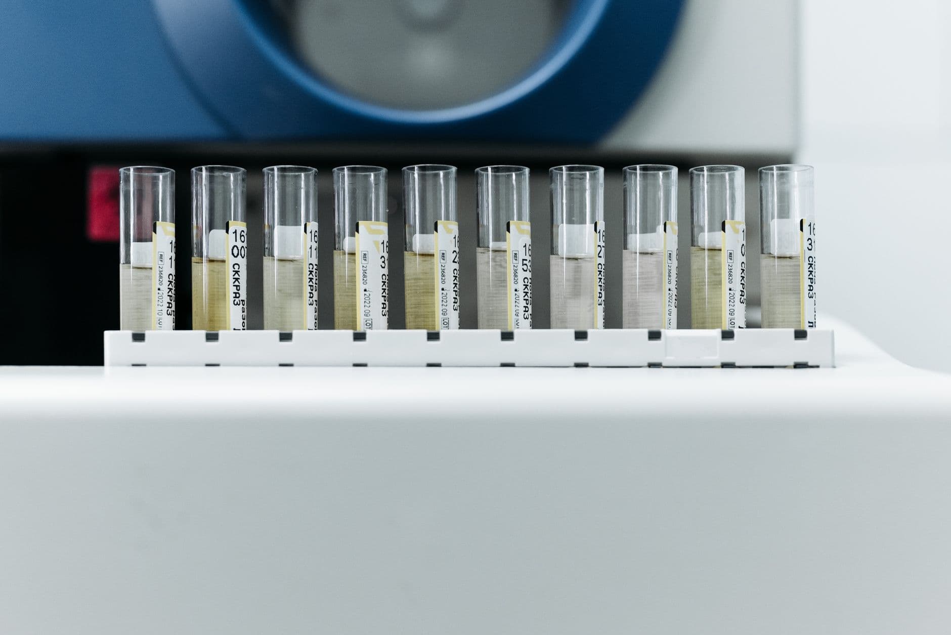 Ti prøverør på rekke i et stativ foran en laboratoriemaskin