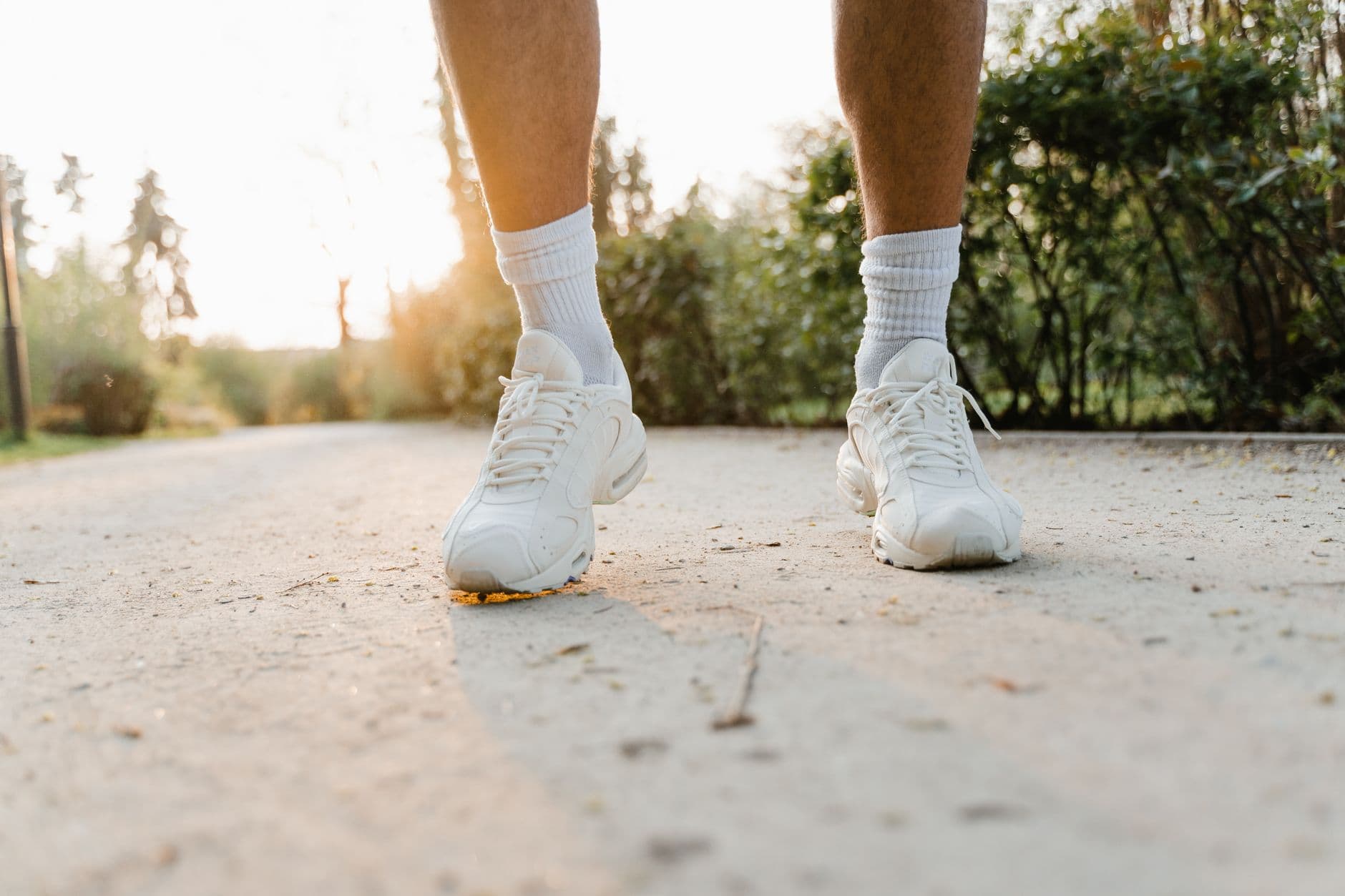 Nærbilde av føtter i lyse sneakers som går på en solfylt sti